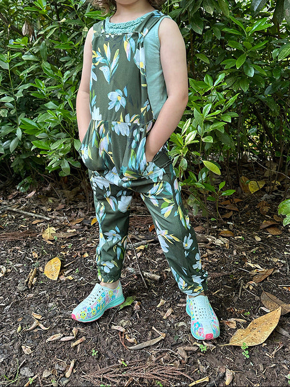 A child standing outdoors wearing a floral print romper.